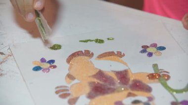 Parlak pudrayla çocuk resimleri yapar. Çocuk kağıt çizimlerini parlak tozla boyuyor, yapıştırıcıya dayanarak küçük parıltıları ovuyor. Çocukların yaratıcılığını geliştirir.