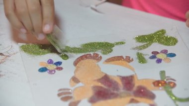 Parlak pudrayla çocuk resimleri yapar. Çocuk kağıt çizimlerini parlak tozla boyuyor, yapıştırıcıya dayanarak küçük parıltıları ovuyor. Çocukların yaratıcılığını geliştirir.