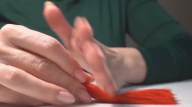 Kadın ellerle mücevher yapıyor. Evde el işi. Bir kadın kendi elleriyle kadınlar için ipliklerden mücevher yapar..