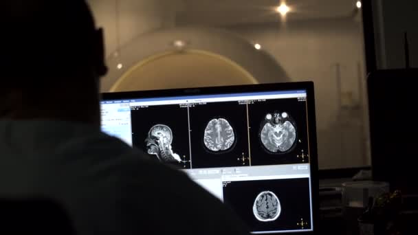 Radiólogo procesa imágenes después de escanear al paciente en la sala de radiología - Mri en el fondo — Vídeo de stock