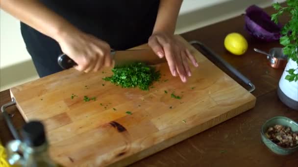 Mujer picando perejil en una mesa de madera en la cocina — Vídeo de stock