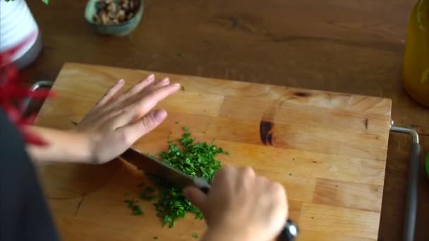 Kvinna hugga persilja på ett träbord i köket — Stockvideo