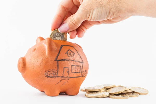 Woman saving money into a traditional clay piggy bank for a house — Stock Photo, Image