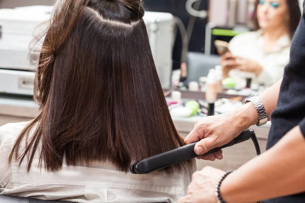 Estilista usando plancha plana en el cabello de cliente femenino —  Fotos de Stock