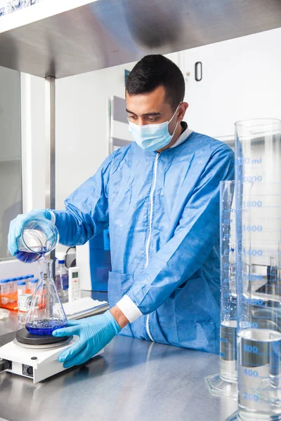 Unga manliga forskare som arbetar med en omrörare på laboratoriet klänning — Stockfoto