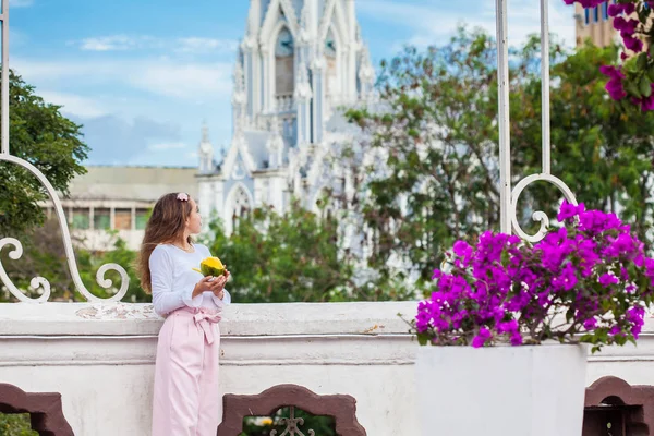 Hermosa joven en el puente de Ortiz comiendo un mango frente a la famosa iglesia gótica de La Ermita construida en 1602 en la ciudad de Cali en Colombia — Foto de Stock