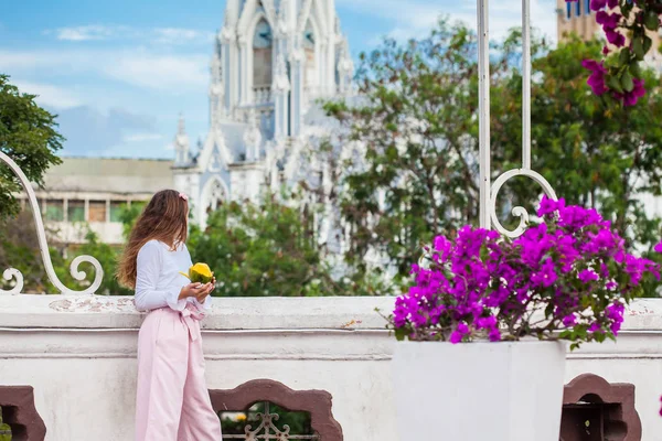 Prachtig jong meisje op de Ortiz brug die een mango eet voor de beroemde gotische kerk van La Ermita gebouwd op 1602 in de stad Cali in Colombia — Stockfoto