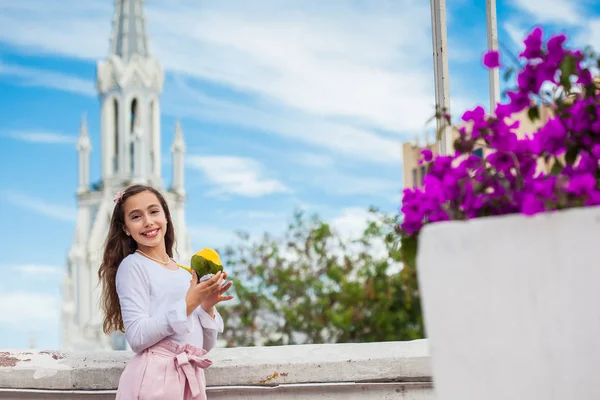 Prachtig jong meisje op de Ortiz brug die een mango eet voor de beroemde gotische kerk van La Ermita gebouwd op 1602 in de stad Cali in Colombia — Stockfoto