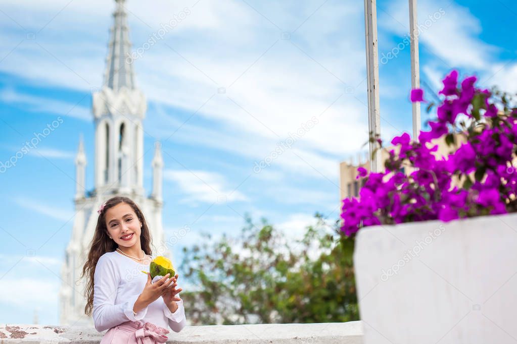 Beautiful young girl on the Ortiz Bridge eating a mango in front of the famous gothic church of La Ermita built on 1602 in the city of Cali in Colombia