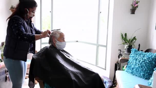 Mujer mayor recibiendo un corte de pelo en casa durante la pandemia de Covid-19 con mascarilla facial — Vídeo de stock