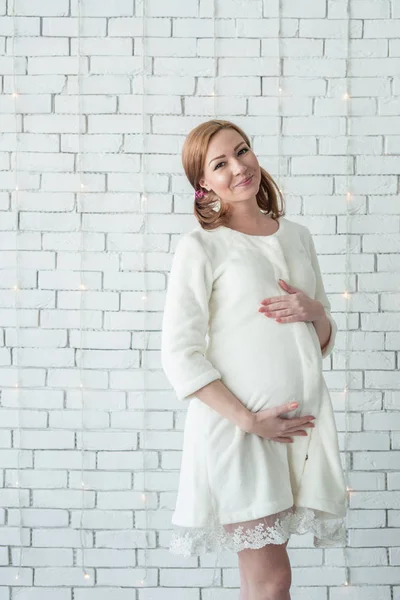 Jeune fille enceinte souriante et debout près du mur blanc — Photo