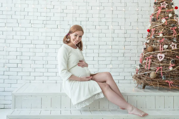 Belle fille enceinte caressant son ventre près du sapin de Noël le matin — Photo