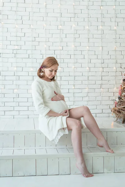 Hermosa chica embarazada acariciando su vientre cerca del árbol de Navidad en la mañana — Foto de Stock