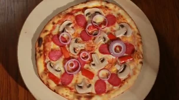 Свежеиспечённая пицца с салями, грибами, луком и перцем оборачивается. Вид сверху — стоковое видео