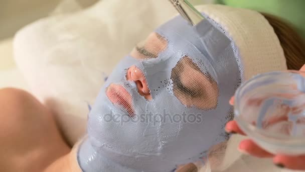 Hermosa mujer joven acostada en la mesa de masaje con máscara facial natural en su cara. Procedimiento de cosmetología femenina — Vídeos de Stock