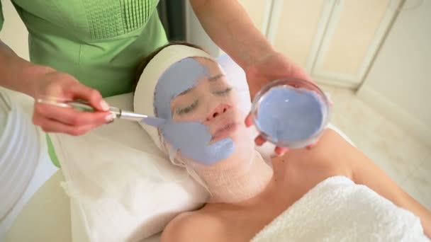 Νεαρή όμορφη γυναίκα σε ένα μπλε μάσκα για το πρόσωπο. Θεραπεία Spa — Αρχείο Βίντεο