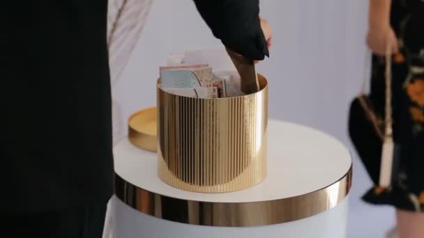 Гості кладуть конверт з грошима в кошик з грошима для молотка і нареченої. Чудова коробка з золотими конусами, наповнена конвертами з грошима. — стокове відео