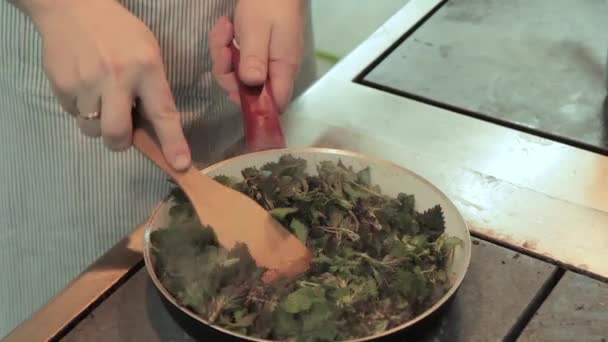 シェフは鍋に鍋の葉をレストランのキッチンに入れます。魚料理のためのニンニクとして鍋にシェフが攪拌し、フライドポテト野生のイラクサ — ストック動画