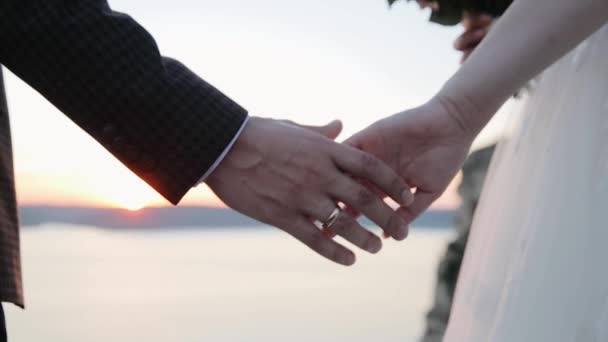 Bröllopspar håller varandra i handen vid solnedgången. Solstrålarna skiner genom fingrarna. Kärlek, lycka och vänskap. Händerna på nära håll vid soluppgången. — Stockvideo