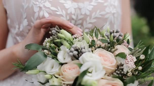 Una giovane sposa in abito bianco esamina e tocca il bouquet da sposa. Steadicam close-up shot, all'aperto — Video Stock