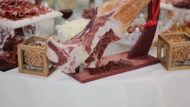 Jamon serrano.Tradicional presunto espanhol no furshet ou banquete. Presunto de perna de porco na mesa. Carne gourmet e lanches diferentes no restaurante. jamon inteiro no carrinho — Vídeo de Stock