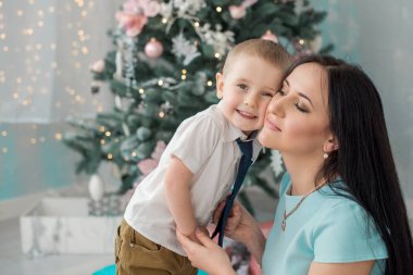 3-4 yıl çocuk hugs annesi arka plan Noel ağacı ve Noel ışıkları. Mutlu bir aile kavramı