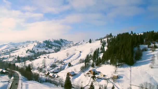 晴れた日の映像の山の下で冬の田園風景の小さな村は、ヘリコプターのカメラで撮影しました。. — ストック動画