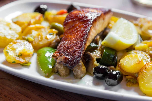 Bir restoranda beyaz bir tabakta sebze ve patates pişmiş somon etli