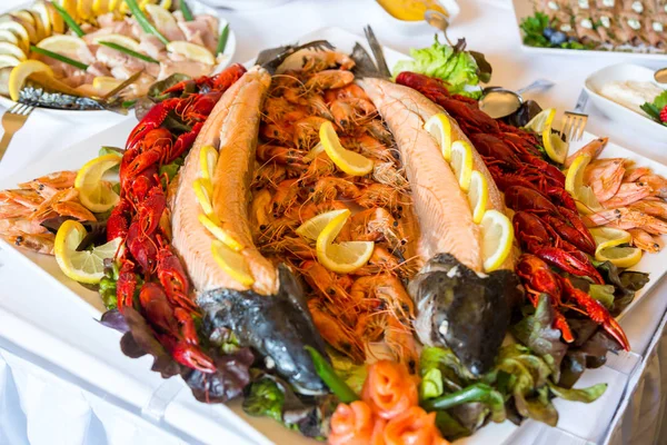 Camarão, lagostim, salmão em uma mesa de buffet decorada com limão, em um prato branco — Fotografia de Stock