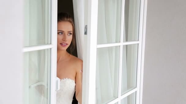 Novia en un vestido blanco mira a través de la ventana — Vídeo de stock