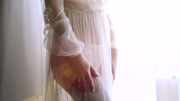 Молода дівчина стоїть біля вікна в нічній сорочці. Ноги крупним планом красивої моделі — стокове відео