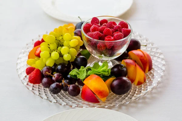 Placa de fruta con frambuesas, uvas y ciruelas está sobre la mesa para dos — Foto de Stock