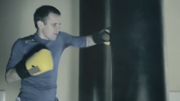 Перед боем спортсмен тренируется. Боксер бьет тяжелую сумку. Чёрный фон — стоковое видео