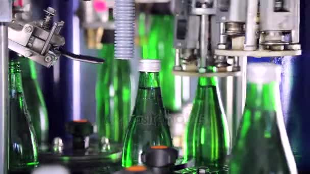 Cubrir automáticamente las botellas con tapas en la planta de agua. Botellas de vidrio verde en línea transportadora automática . — Vídeo de stock