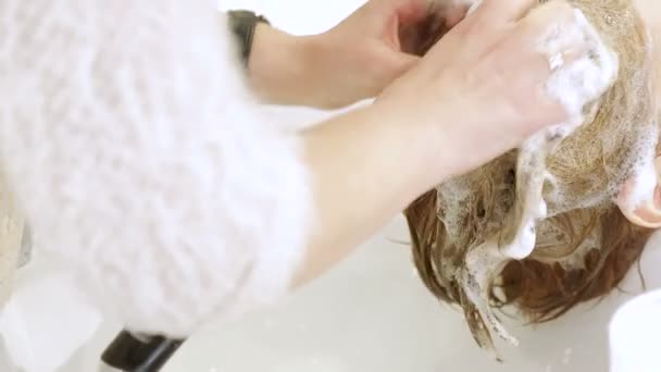 O cabeleireiro limpa suavemente o cabelo com um xampu em um salão de beleza . — Vídeo de Stock