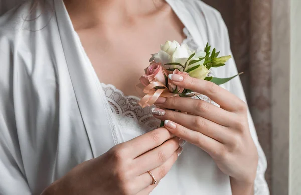 Gentle hand of the bride holding boutonniere for the groom. Bride holding a buttonhole