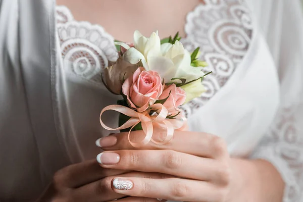 Gentle hand of the bride holding boutonniere for the groom. Bride holding a buttonhole