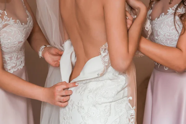 Bridesmaids help dress up a wedding dress. The bride is wrapped back to the camera, demonstrating her exquisite back — Stock Photo, Image