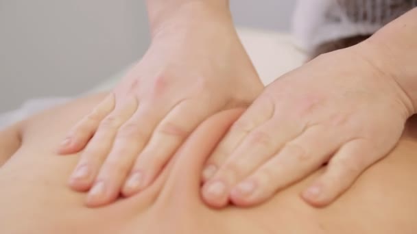 Закрывай. Массажистка делает массаж тела, нежно массируя спину в салоне красоты — стоковое видео