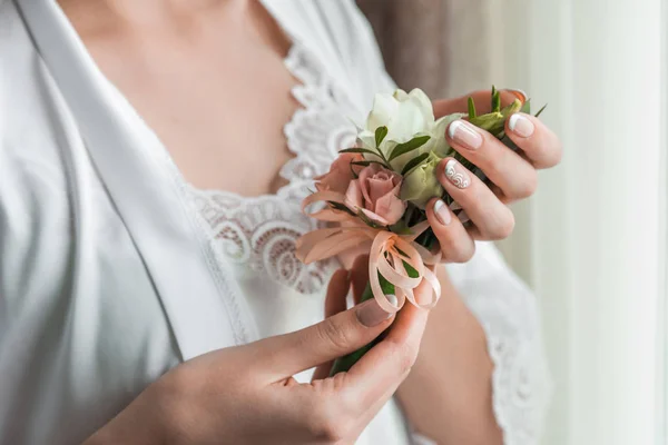 Mano gentil de la novia sosteniendo boutonniere para el novio. Novia sosteniendo un ojal — Foto de Stock