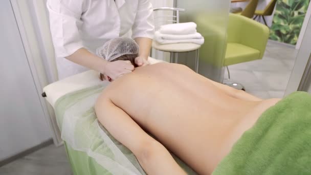 Masajista realiza masajes del cuerpo, masajeando suavemente su espalda en el salón de belleza — Vídeo de stock