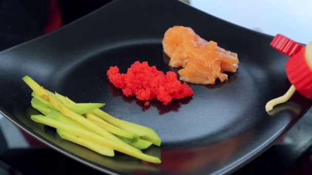 Koch aus nächster Nähe stellt einen Teller mit Sushi-Zutaten auf den Tisch. Zutaten für Sushi, Avocado und roten Fisch — Stockvideo