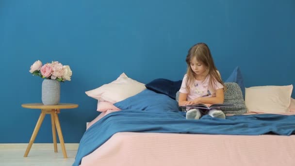 Uma menina está lendo um livro na cama . — Vídeo de Stock