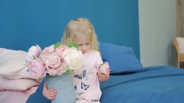 Menina segurando um vaso grande com flores e joga-los em seu quarto na cama — Vídeo de Stock