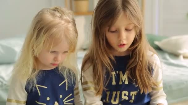 Дві маленькі дівчата в світлій кімнаті з рослинами, читають книгу — стокове відео