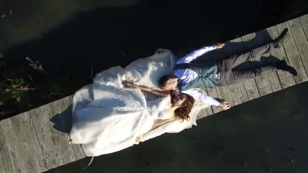 Brides are lying on a small bridge in the park. Aerial view on top. Filming a dron, the camera flies away from the brides — Stock Video