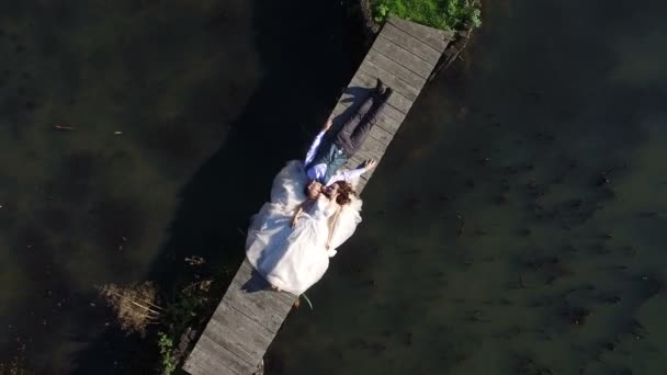 Brides are lying on a small bridge in the park. Aerial view on top. Filming a dron, the camera flies away from the brides — Stock Video