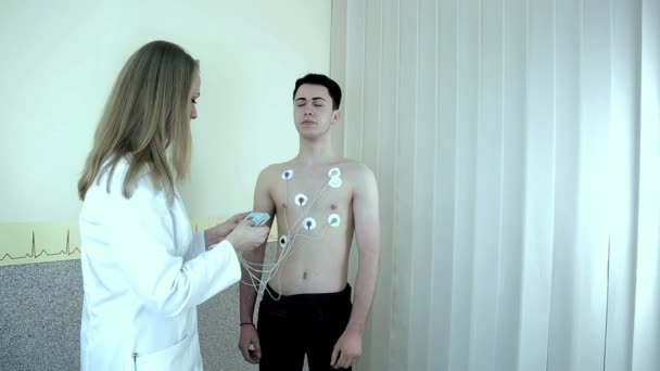 Der Arzt berät einen jungen Patienten mit Herzkrankheiten. der Arzt wird angewiesen, den Halter zu benutzen — Stockvideo