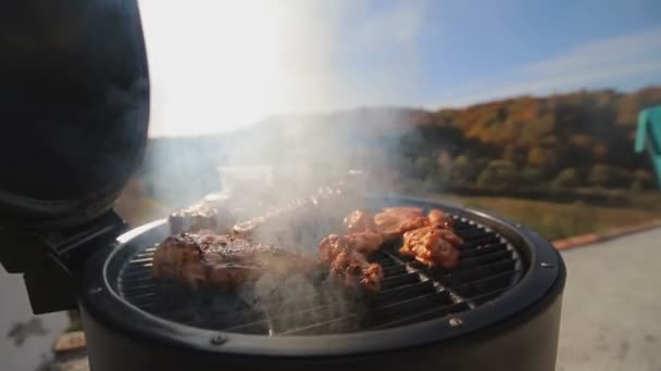 Fleischstücke, Huhn, Rippchen, auf dem Feuer gebraten. Kochen von Grillfleisch auf dem Dach des Hauses, vor einem schönen Panorama. — Stockvideo
