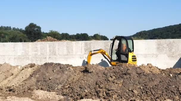 Ein gelber Minibagger gräbt auf einer Baustelle ein Loch. Ein kleiner Bagger zieht die Erde aus der Grube. — Stockvideo